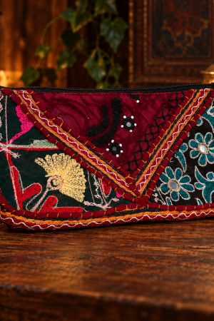 Bolsa de mão bordô e verde com bordados florais e geométricos, zíper preto e detalhes pendentes coloridos, vista de frente